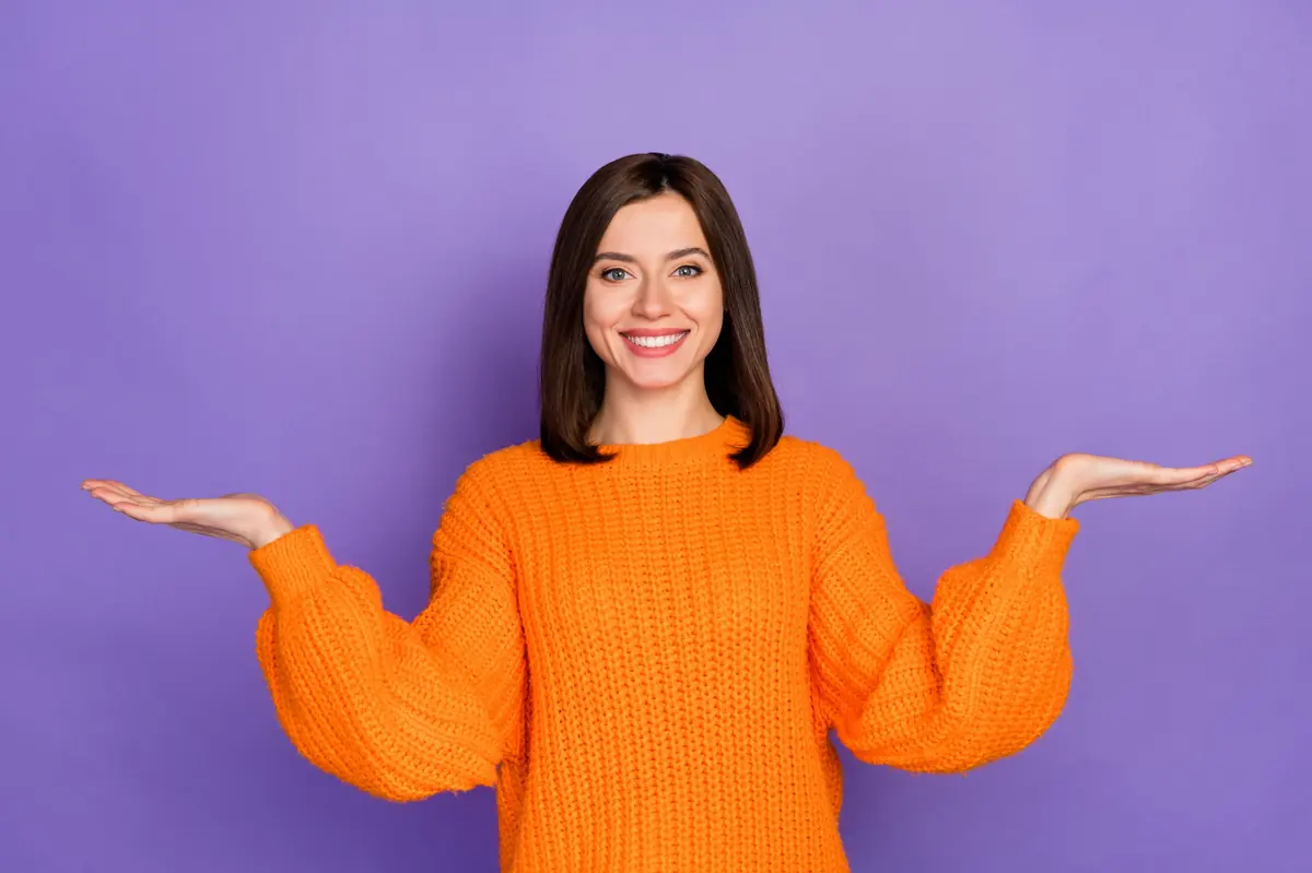 A smiling woman weighing two options, one in each open hand