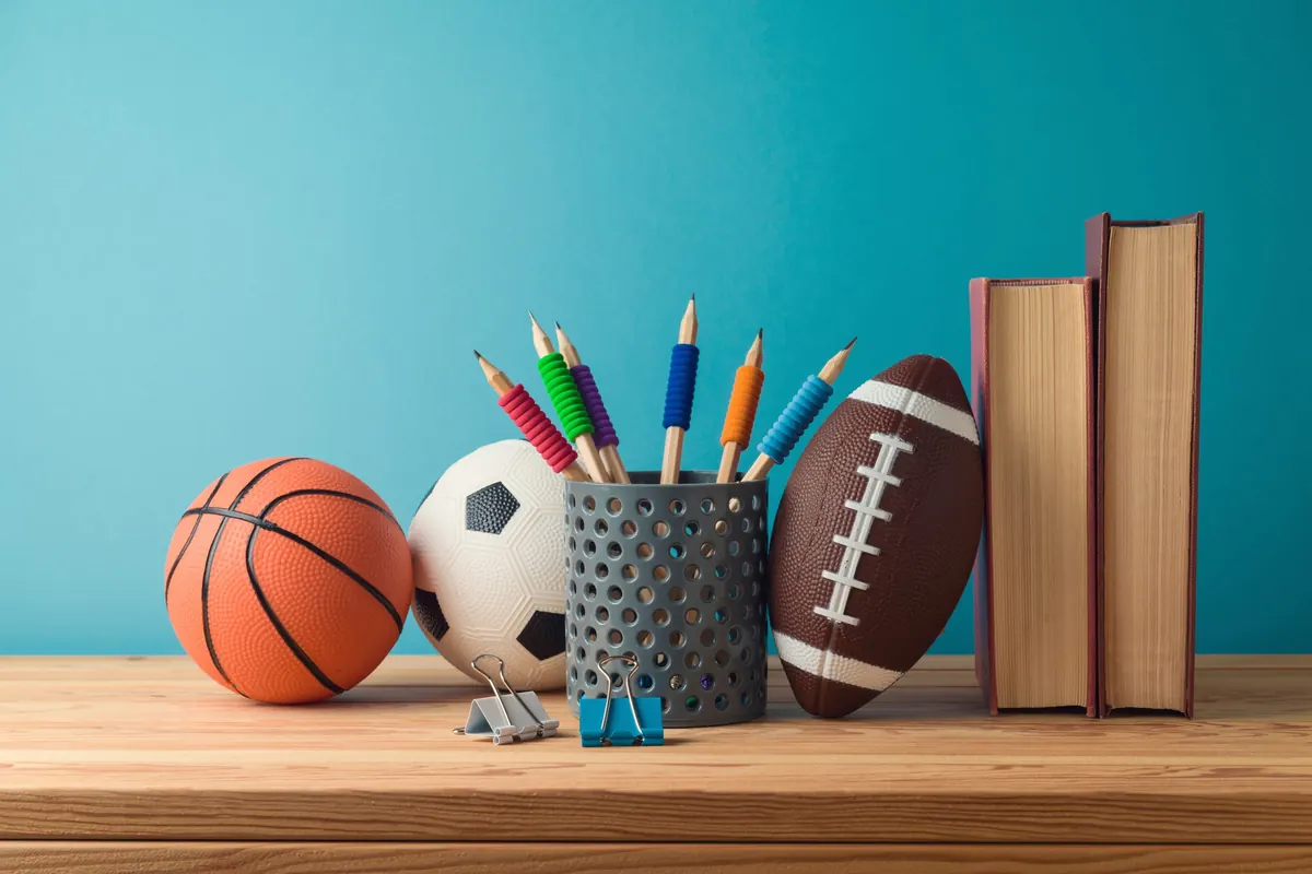 A basketball, a soccer ball and a football on a desk beside a stack of books